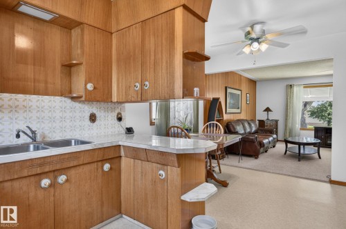 Wood-finish cabinetry in a kitchen space featuring a double basin stainless steel sink, patterned tile backsplash, and a breakfast bar - 12908 104 Street Nw, Edmonton, AB - Indoor Photo Showing Kitchen With Double Sink