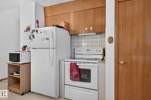 Kitchen area featuring wood-finish upper cabinetry, white appliances, and a patterned tile backsplash - 12908 104 Street Nw, Edmonton, AB - Indoor