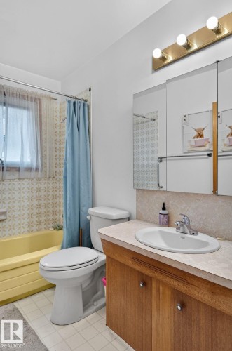 Bathroom featuring a yellow bathtub, patterned wall tile, and a vanity with a white countertop and wood-finish cabinetry - 12908 104 Street Nw, Edmonton, AB - Indoor Photo Showing Bathroom