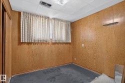 Room featuring wood-finish paneling, a dropped ceiling with recessed lighting, and a window with patterned curtains - 