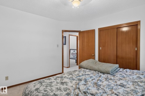 Interior room featuring a ceiling-mounted light fixture, warm wood-finish trim, a solid wood-finish door, and a closet with sliding wood-finish doors - 12908 104 Street Nw, Edmonton, AB - Indoor Photo Showing Bedroom