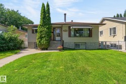 Front elevation featuring a stucco exterior with a stone-finish foundation, mature front yard landscaping, concrete walkway, and a covered entry - 