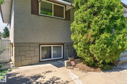 Exterior facade featuring a textured stucco finish, a lower level of stone-patterned siding, and white-framed windows - 