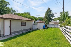 Expansive backyard featuring a manicured lawn, white picket fence, and a detached structure with shingled roof - 