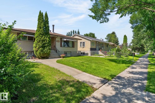 Exterior featuring stucco siding, stone facade accents, mature landscaping, a concrete sidewalk, and a lush green lawn - 12908 104 Street Nw, Edmonton, AB - Outdoor