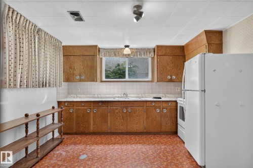 Kitchen featuring wood cabinetry, light-toned countertops, a tiled backsplash, and patterned flooring - 12908 104 Street Nw, Edmonton, AB - Indoor Photo Showing Kitchen