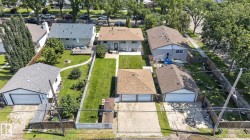 Rear exterior featuring a spacious green lawn, mature trees, a wooden deck, and a detached two-car garage with a brown shingle roof - 