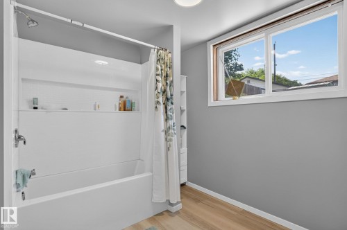 White shower-over-tub combination with integrated shelving, chrome fixtures, and wood-finish flooring - 12908 104 Street Nw, Edmonton, AB - Indoor