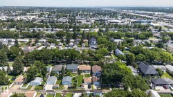 Expansive aerial perspective showcasing a residential neighborhood with numerous detached homes, mature trees, and a distant commercial/industrial area - 