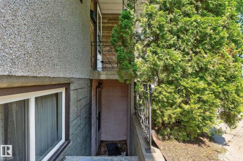 Exterior featuring a gravel-textured facade, brick accents, and a lower-level entrance with a window - 12908 104 Street Nw, Edmonton, AB - Outdoor