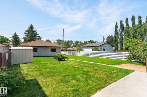 Spacious backyard featuring a manicured lawn, a white ranch-style fence, a storage shed, and mature perimeter trees - 12908 104 Street Nw, Edmonton, AB - Outdoor