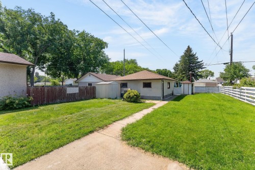 Spacious backyard featuring a concrete pathway, a detached storage shed, a white picket fence, a brown wood fence, and mature trees - 12908 104 Street Nw, Edmonton, AB - Outdoor