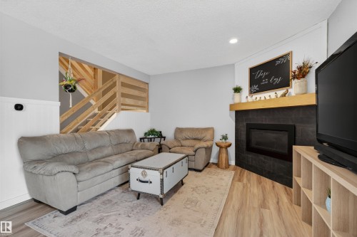 Living area featuring wood-finish flooring and a corner fireplace with dark tile surround and a light wood mantel - 18116 81 Avenue, Edmonton, AB 