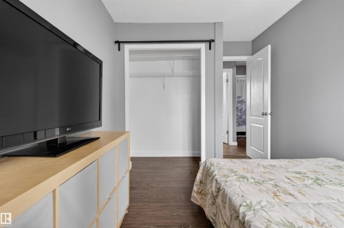 Bedroom featuring dark wood-finish flooring, a white trim baseboard, and a closet with a black metal rod - 18116 81 Avenue, Edmonton, AB 