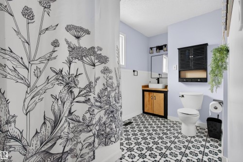 Bathroom featuring patterned floor tiles, a wood-finish vanity with a vessel sink, a wall-mounted medicine cabinet, modern black fixtures, and a shower area - 18116 81 Avenue, Edmonton, AB 