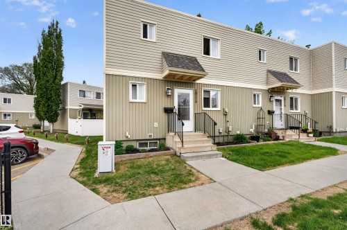 Multi-unit residential building featuring two stories of siding, a covered entrance with exterior lighting, and a front yard with grass and concrete walkways - 18116 81 Avenue, Edmonton, AB 