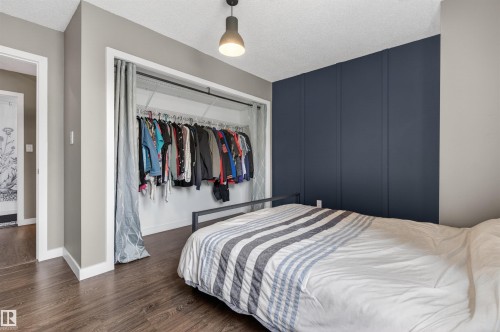 Bedroom featuring dark wood-finish flooring, a contemporary dark accent wall, and a built-in closet with shelving and hanging rods - 18116 81 Avenue, Edmonton, AB 