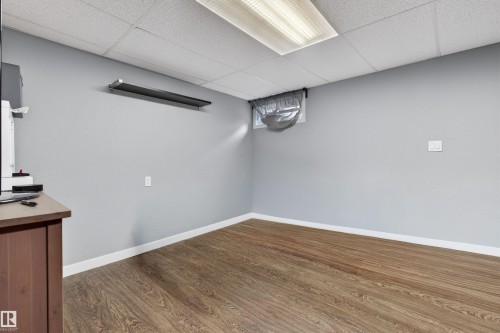 Spacious room featuring wood-finish flooring, light gray walls, and white baseboards - 18116 81 Avenue, Edmonton, AB 