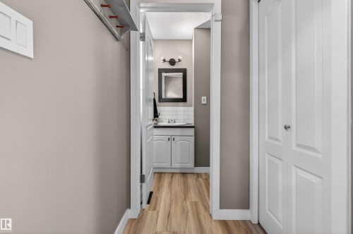 Bathroom entry featuring wood-finish flooring, white subway tile backsplash, a dark vanity mirror, and a two-light wall sconce - 18116 81 Avenue, Edmonton, AB 