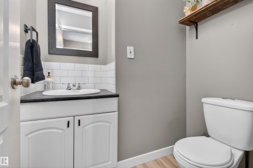 Powder room featuring a white pedestal toilet, corner vanity with a dark countertop, white subway tile backsplash, and a dark framed mirror - 18116 81 Avenue, Edmonton, AB 