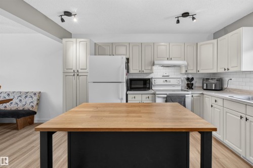 Kitchen featuring a central island with a wood-finish countertop, white cabinetry with dark hardware, white subway tile backsplash, and wood-finish flooring - 18116 81 Avenue, Edmonton, AB 