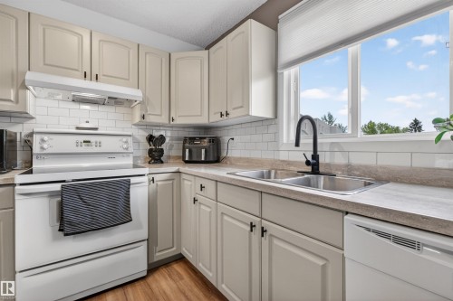 Kitchen featuring light-toned cabinetry with dark hardware, a white subway tile backsplash, and wood-finish flooring - 18116 81 Avenue, Edmonton, AB 
