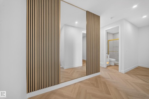 Herringbone wood-finish flooring complements a feature wall with vertical wood slat detailing and an integrated full-length mirror - 2808 191 Street Nw, Edmonton, AB - Indoor Photo Showing Other Room
