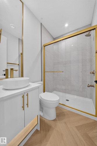 Contemporary bathroom featuring a glass-enclosed shower with gold-finish trim, a round white vessel sink, gold-finish faucet, and wood-finish flooring in a herringbone pattern - 2808 191 Street Nw, Edmonton, AB - Indoor Photo Showing Bathroom