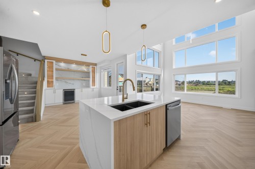 Modern kitchen featuring a waterfall island with a double sink, light wood-finish cabinetry, and stainless steel appliances - 2808 191 Street Nw, Edmonton, AB - Indoor Photo Showing Kitchen With Double Sink