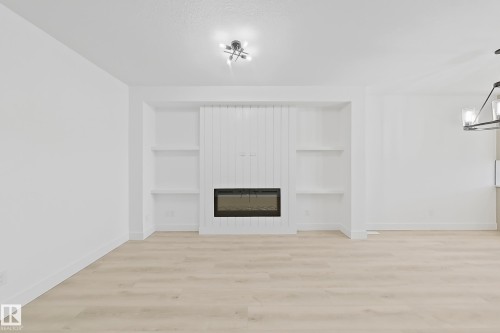 Living area featuring a modern fireplace with a vertical shiplap surround, built-in shelving, wood-finish flooring, and crisp white walls - 4215 63 Street, Beaumont, AB - Indoor With Fireplace