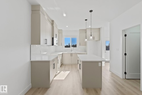 Modern kitchen featuring an island with pendant lighting, light wood-finish flooring, white countertops, and a subway tile backsplash - 4215 63 Street, Beaumont, AB - Indoor Photo Showing Kitchen With Upgraded Kitchen