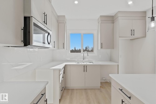 Modern kitchen featuring light cabinetry with dark hardware, a stainless steel over-the-range microwave, crisp white countertops, and a full-height backsplash - 4215 63 Street, Beaumont, AB - Indoor