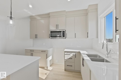 Bright kitchen featuring white cabinetry, a built-in microwave, a double basin sink, ample counter space, and light wood-finish flooring - 4215 63 Street, Beaumont, AB - Indoor Photo Showing Kitchen With Double Sink With Upgraded Kitchen