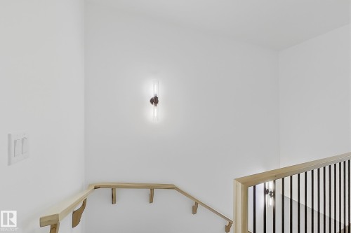 Modern wall sconce lighting illuminates the staircase, featuring light wood handrails and black metal balusters - 4215 63 Street, Beaumont, AB - Indoor Photo Showing Other Room