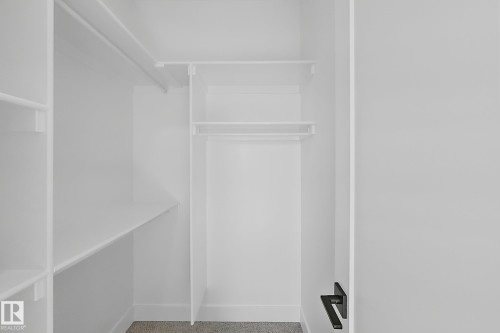 White closet system featuring multiple shelves and hanging rods, complemented by a gray carpeted floor and a matte black door handle - 4215 63 Street, Beaumont, AB - Indoor With Storage