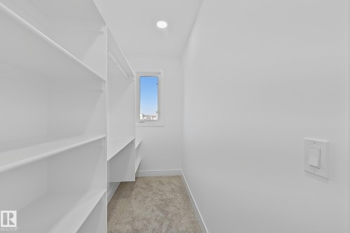 Walk-in closet featuring extensive built-in shelving, hanging rods, and a window for natural illumination - 4215 63 Street, Beaumont, AB - Indoor