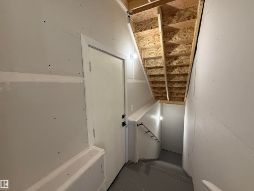 Unfinished basement stairway featuring plywood treads and risers, drywall walls, and a white handrail - 4215 63 Street, Beaumont, AB - Indoor