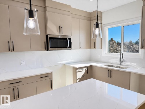 Modern kitchen featuring a large island, sleek cabinetry, quartz countertops, a stainless steel microwave, and pendant lighting fixtures - 4215 63 Street, Beaumont, AB - Indoor Photo Showing Kitchen