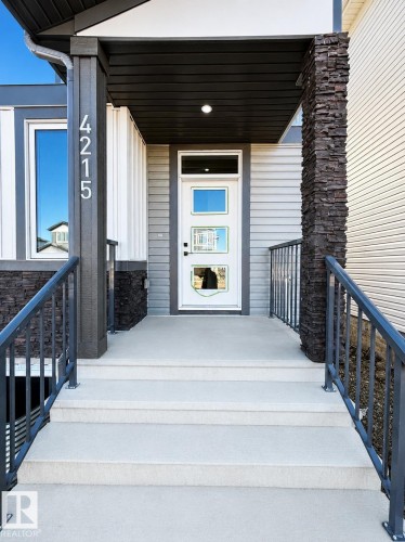 Modern entry featuring a white door with three vertical glass panels, dark grey siding, and contrasting light grey siding - 4215 63 Street, Beaumont, AB - Outdoor With Exterior