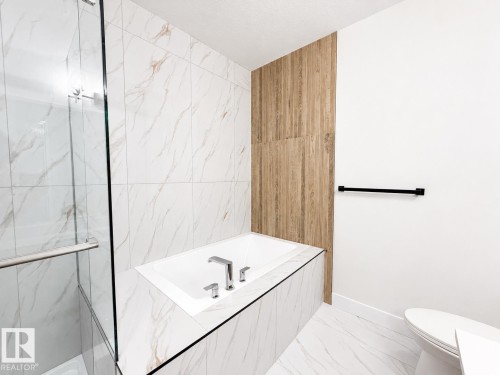 Soaking tub with deck-mounted chrome fixtures, surrounded by large format tile with subtle veining - 4215 63 Street, Beaumont, AB - Indoor Photo Showing Bathroom
