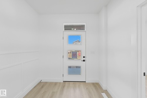 Modern entry door with three square lites and transom window, wood-finish flooring, white baseboards, and wainscoting detail - 4215 63 Street, Beaumont, AB - Indoor Photo Showing Other Room