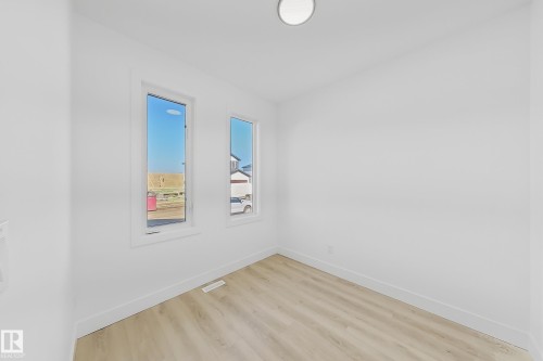 Bright room featuring two vertical windows, wood-finish flooring, white baseboards, and a flush-mount ceiling light - 4215 63 Street, Beaumont, AB - Indoor Photo Showing Other Room