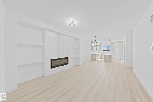 Open-concept living area featuring light wood-finish flooring, recessed lighting, and a built-in electric fireplace with vertical paneling - 4215 63 Street, Beaumont, AB - Indoor With Fireplace