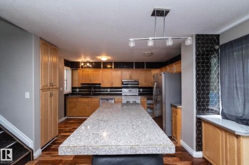 Kitchen featuring a large granite-look island, wood-finish flooring, light wood cabinetry, a black subway tile backsplash, and a black geometric tile accent wall - 11915 77 Street Nw, Edmonton, AB - Indoor