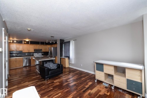 Open-concept living space featuring wood-finish flooring, a kitchen with stainless steel appliances, a center island, and natural wood cabinetry - 11915 77 Street Nw, Edmonton, AB - Indoor