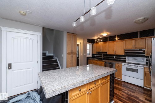 Kitchen featuring wood-finish flooring, a central island with a light-toned countertop, natural wood cabinetry, and a dark tiled backsplash - 11915 77 Street Nw, Edmonton, AB - Indoor Photo Showing Kitchen