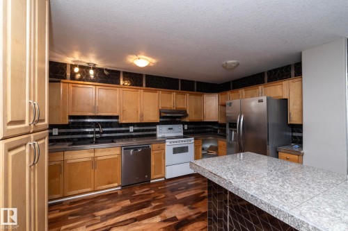 Kitchen featuring wood-finish flooring, a white electric range, and a stainless steel refrigerator - 11915 77 Street Nw, Edmonton, AB - Indoor Photo Showing Kitchen