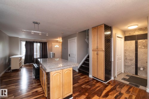 Open-concept room featuring wood-finish flooring, a kitchen island with a stone-finish countertop, and light wood cabinetry - 11915 77 Street Nw, Edmonton, AB - Indoor Photo Showing Kitchen