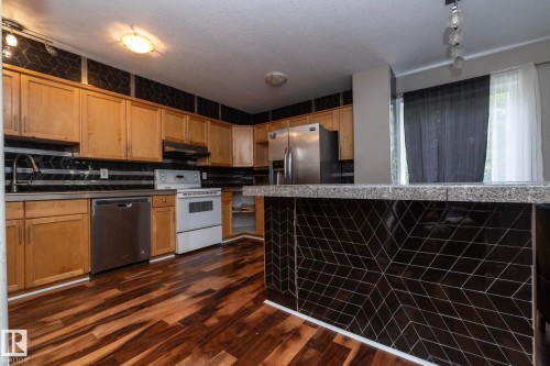 Kitchen featuring wood-finish flooring, natural wood cabinetry, and a black geometric-patterned backsplash - 11915 77 Street Nw, Edmonton, AB - Indoor Photo Showing Kitchen