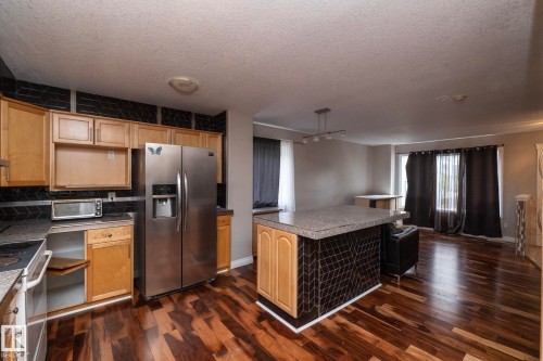Kitchen with wood-finish flooring, light wood cabinetry, and a black patterned tile backsplash - 11915 77 Street Nw, Edmonton, AB - Indoor Photo Showing Kitchen
